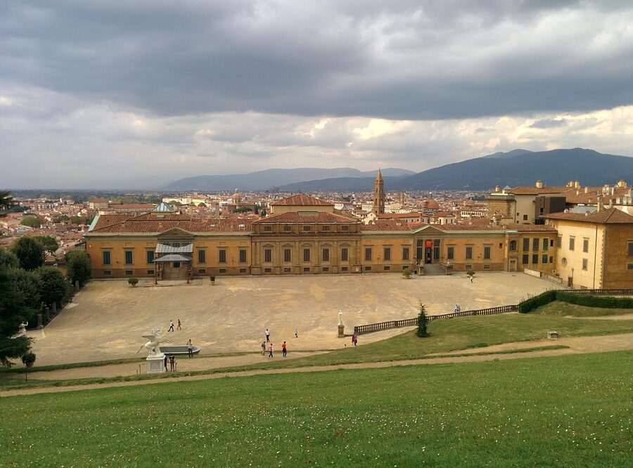 Large green lawn in front of Pitti Palace in Florence with people relaxing under cloudy sky