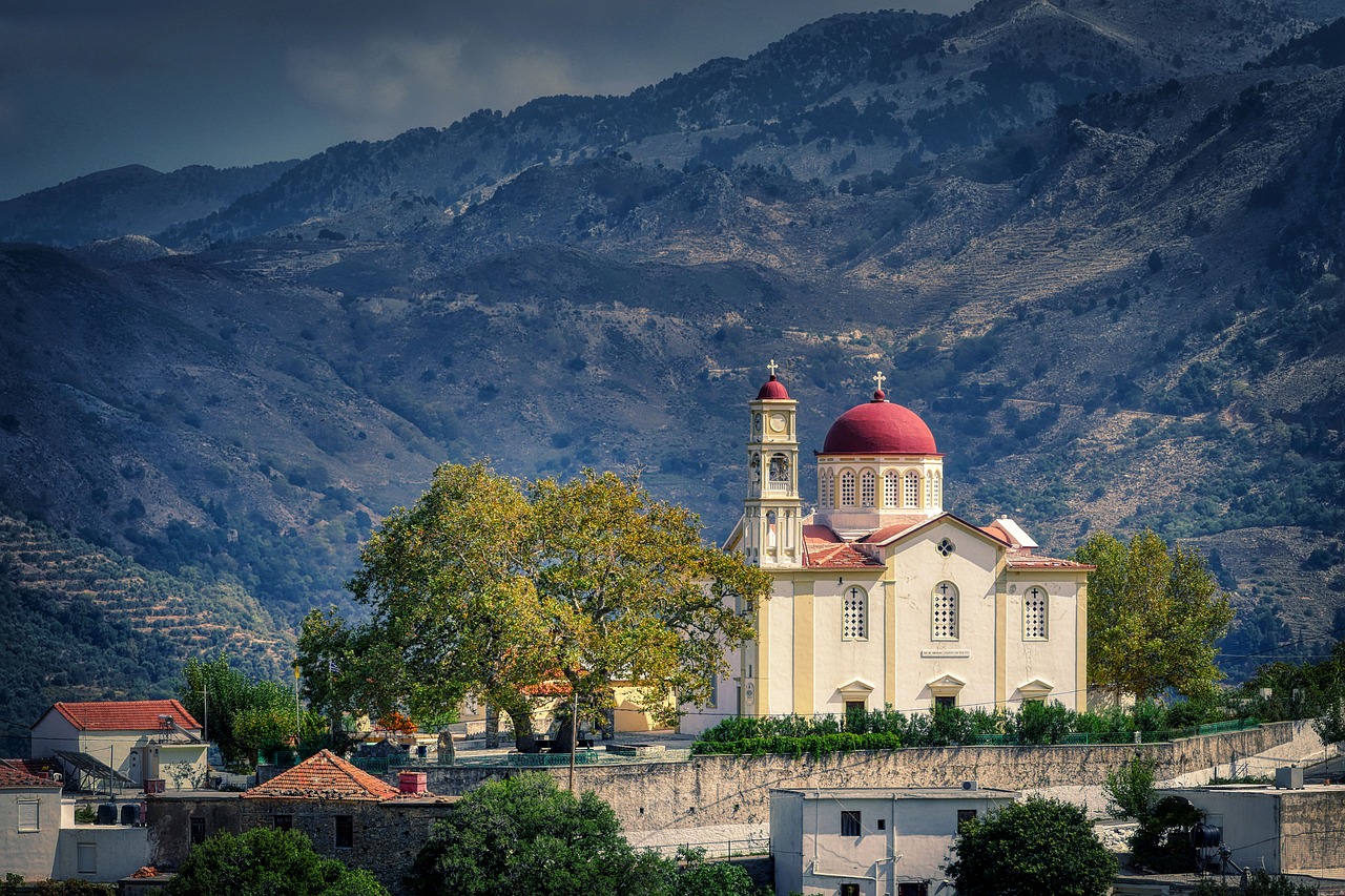 A white monastery with a bell tower set against dramatic mountains in Crete Greece