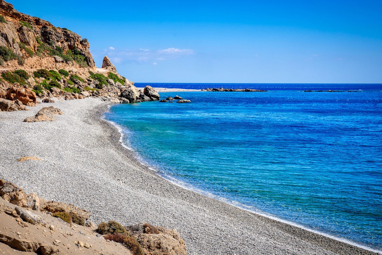 A pebbly beach on the coast of Crete with mountains and hikers visible