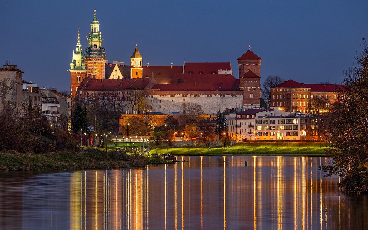 Wawel Royal Castle illuminated at night with the Vistula River in the foreground