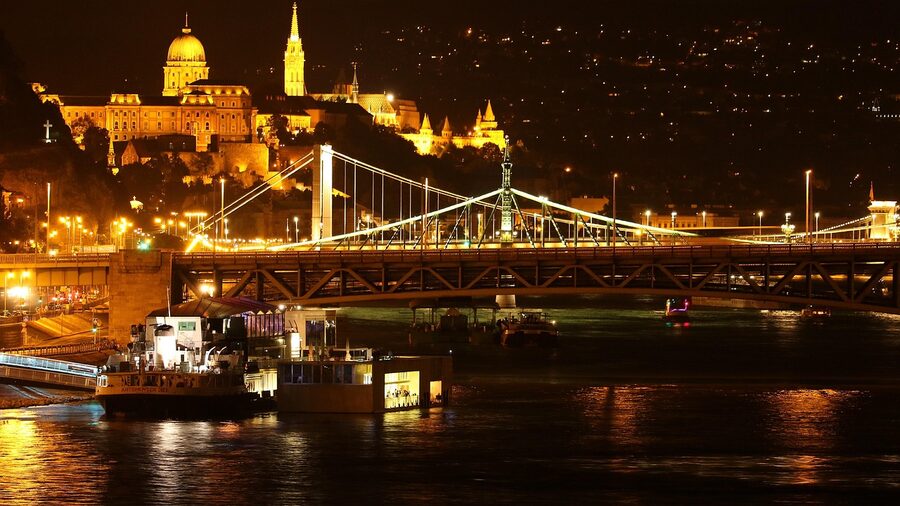 Budapest bridges and buildings illuminated at night viewed from the Danube riverbank