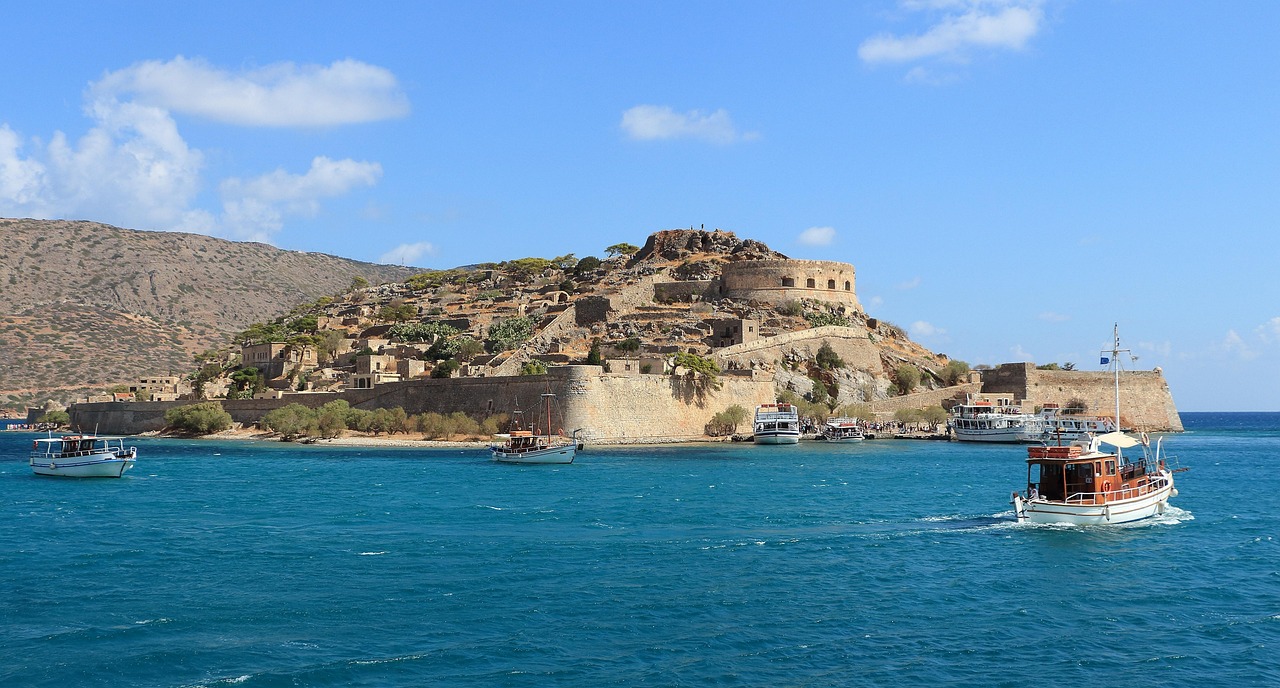 Boats approaching Spinalonga Island with the fortress and ruins visible on the hillside