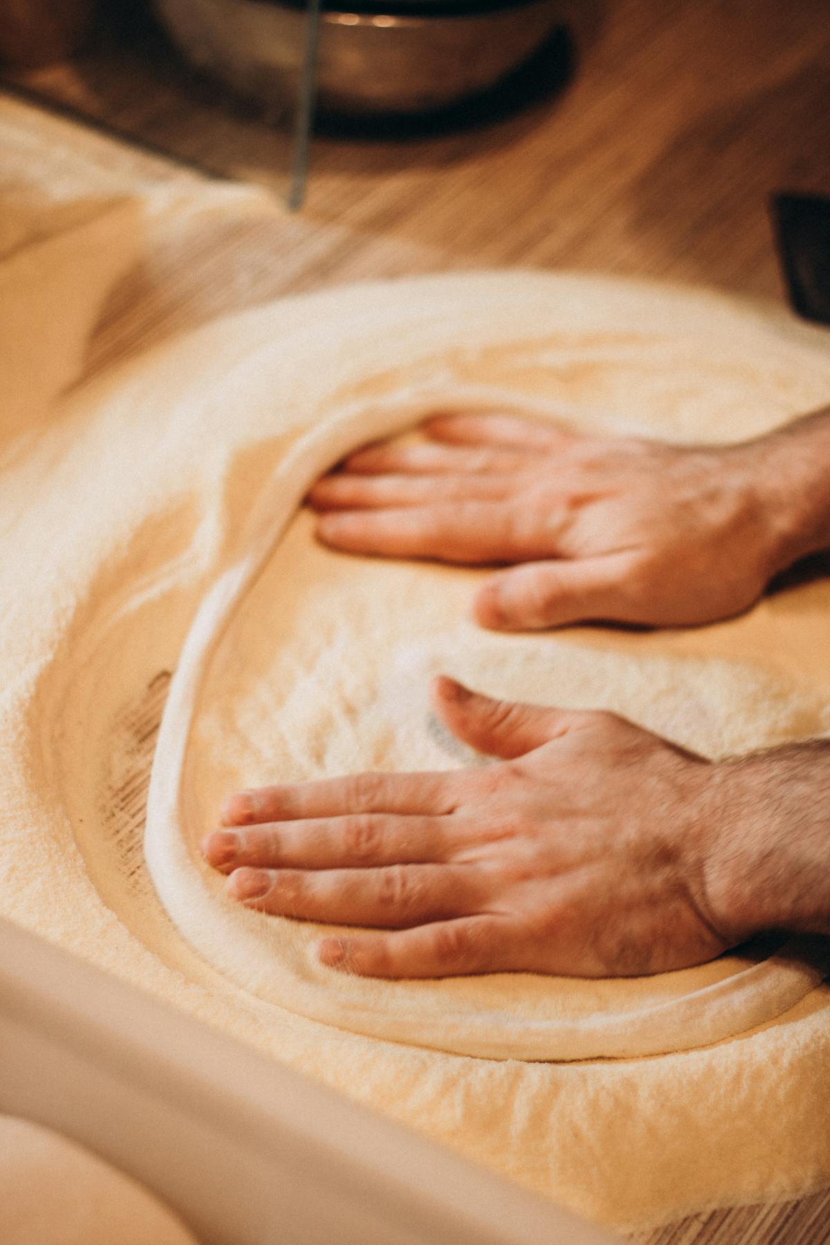 Close-up of hands kneading pizza dough on a floured surface