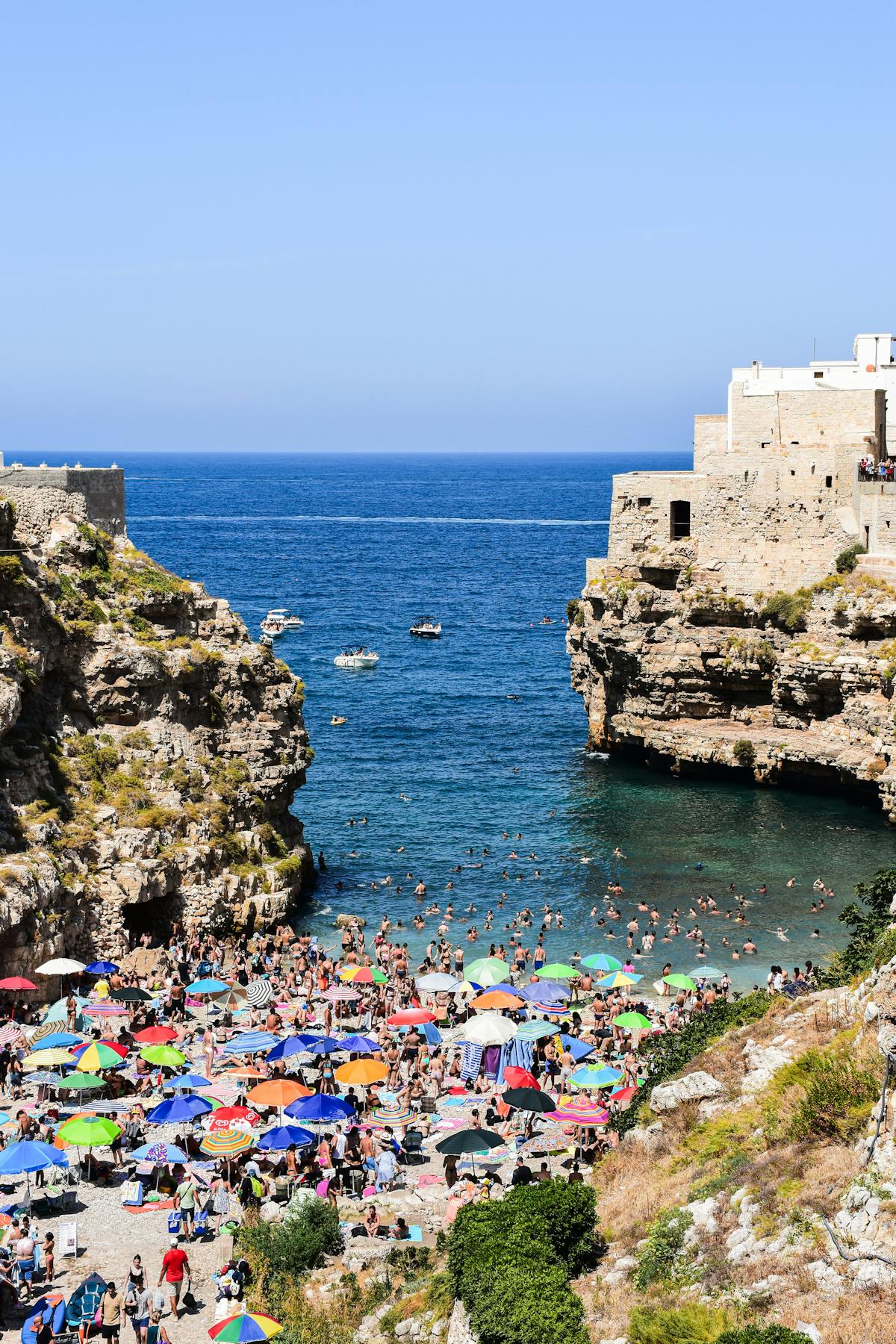 Tourists enjoying the beach at Polignano a Mare on a bright summer day with turquoise water