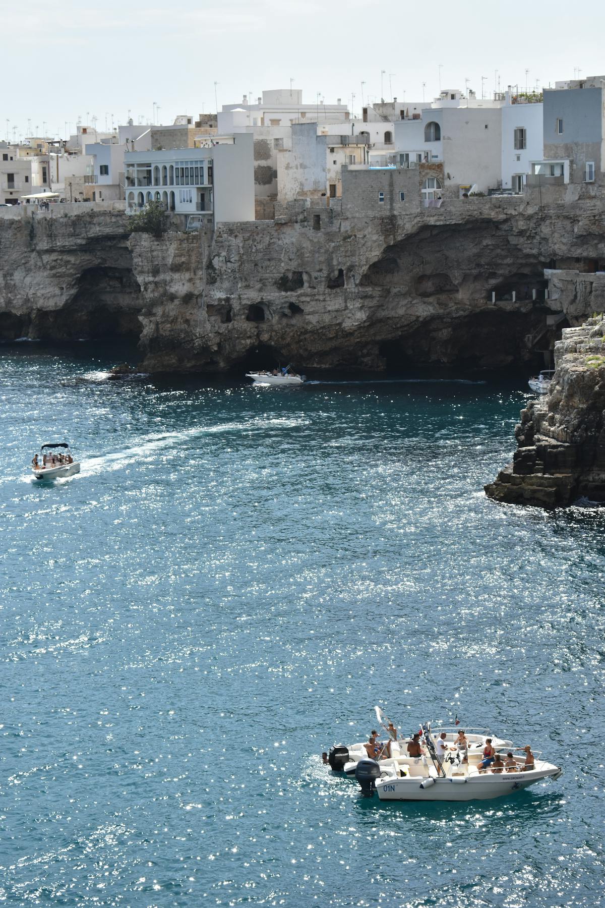 Small boats floating near the rocky coastline of Polignano a Mare with cliffs in the background