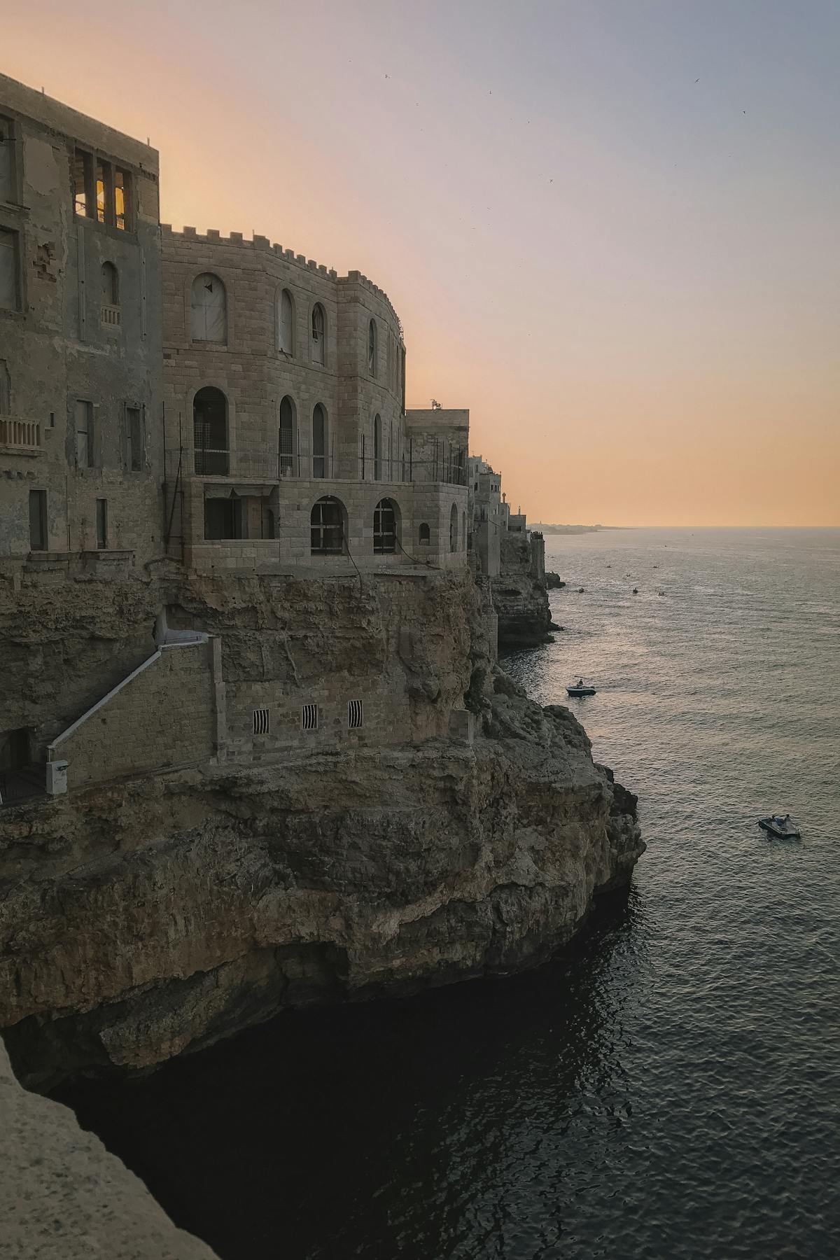 The cliffs and buildings of Polignano a Mare lit by warm sunset light