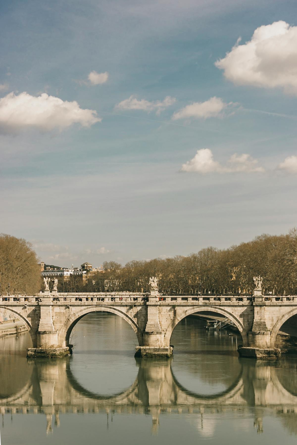 Ponte Sant'Angelo bridge reflecting in the Tiber River under a calm sky