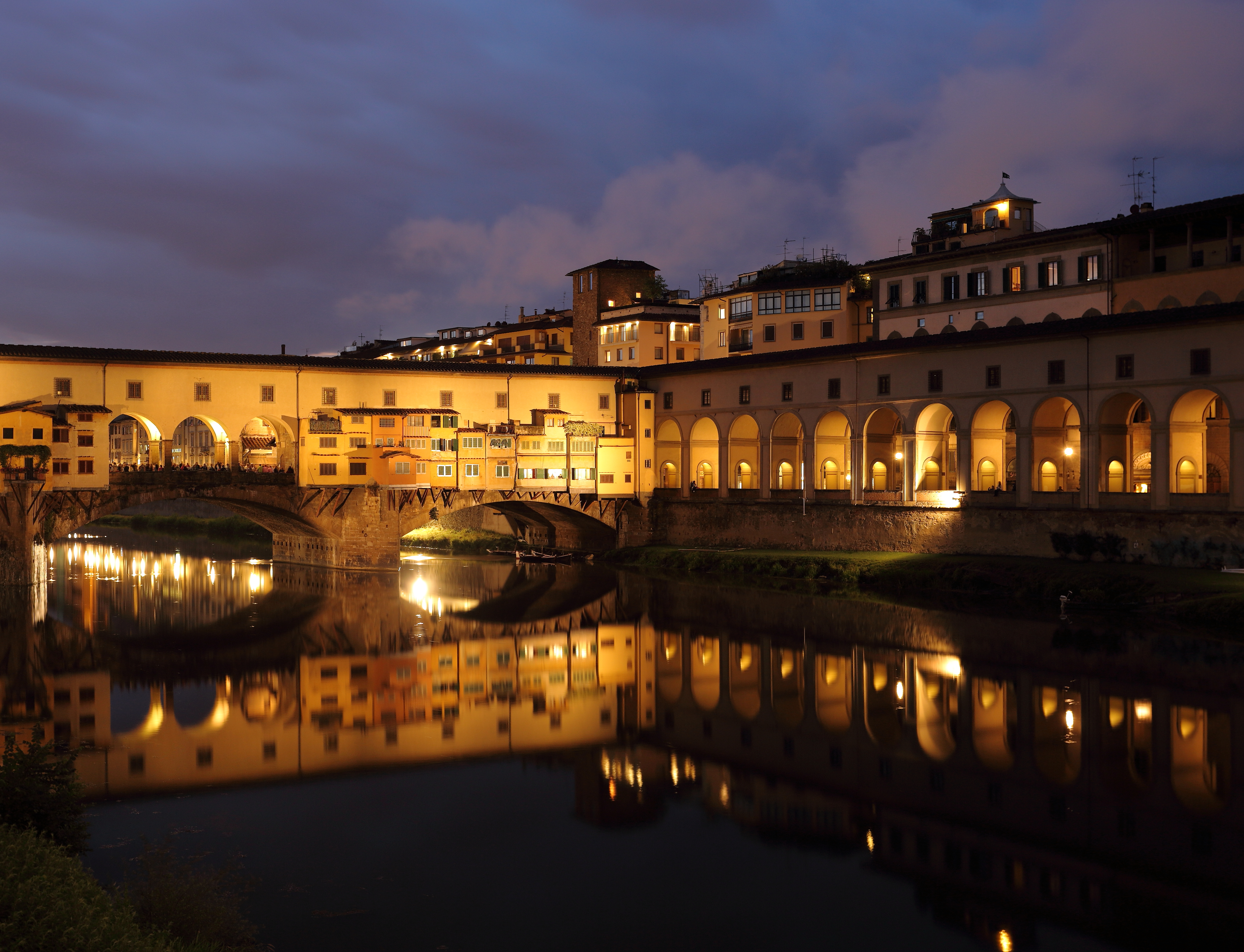 Ponte Vecchio bridge in Florence at dusk with warm lights reflected in the Arno River