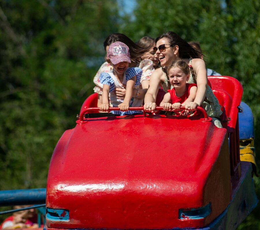 Children and adults enjoying a red roller coaster ride at amusement park
