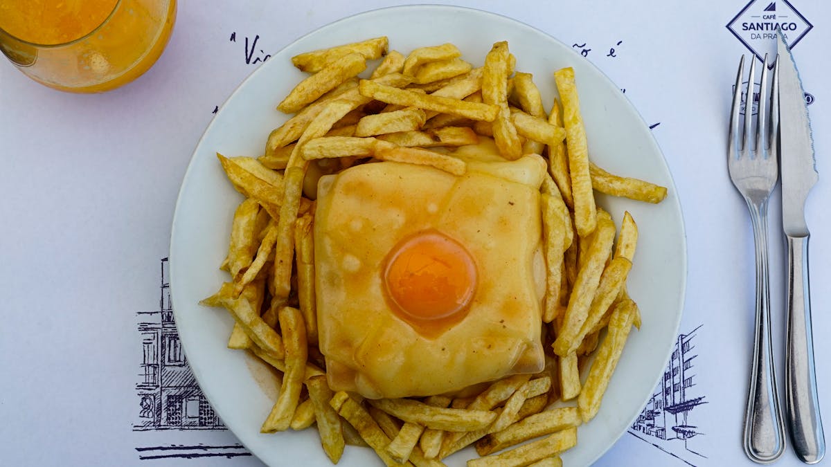 Francesinha sandwich topped with melted cheese and egg, served with fries