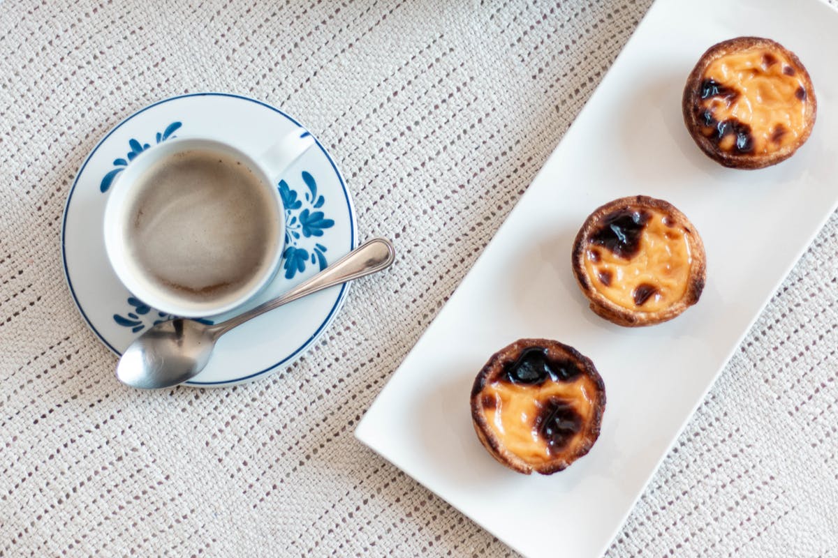 Cup of espresso with three custard tarts on a lace tablecloth