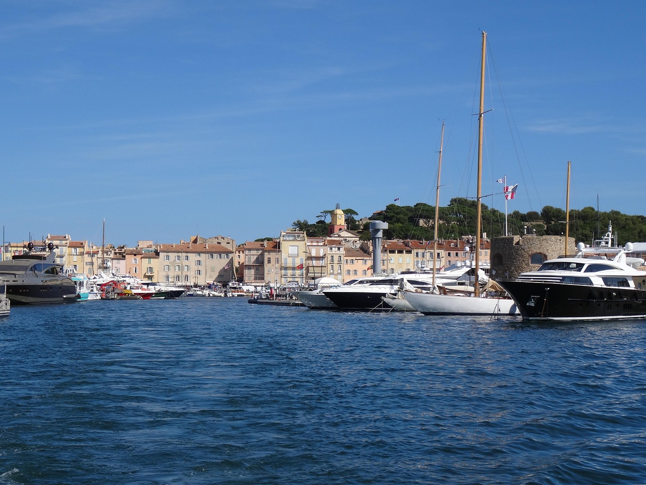 Sailing yachts and motorboats moored in the Saint-Tropez marina with town buildings behind