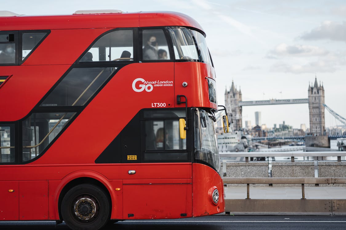 Red double-decker bus driving along the Thames with Tower Bridge in the background