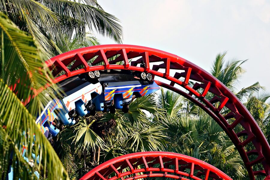 Red roller coaster track winding through palm trees at a theme park