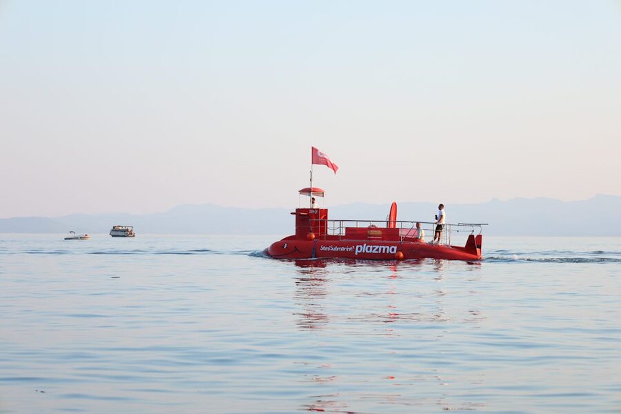 Red semi-submarine sailing on calm blue sea with mountains in background