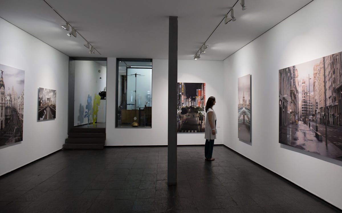 Woman looking at urban landscape paintings displayed in a Madrid art gallery