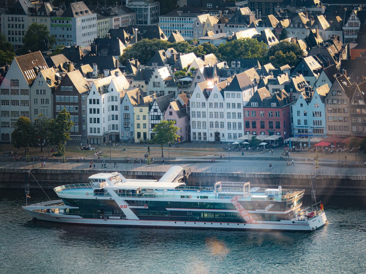 Sunny day at Cologne riverside with colorful houses and a cruise boat on the river