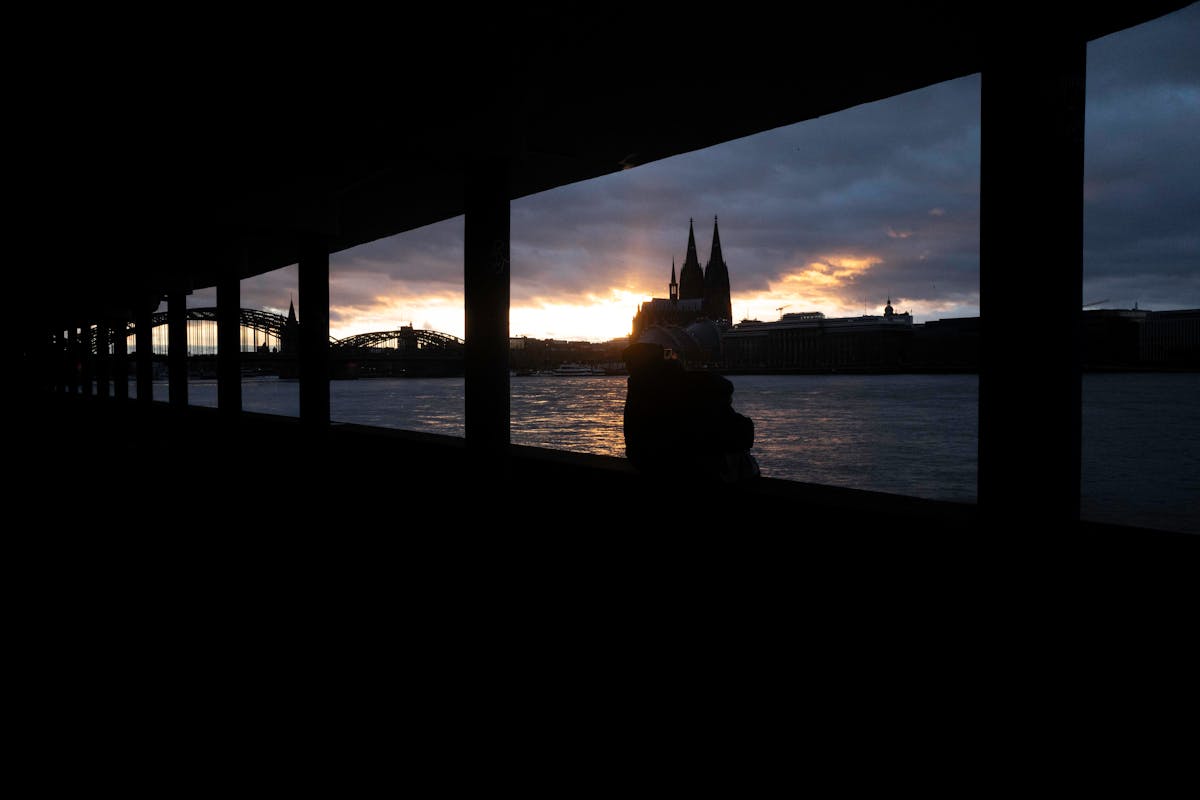 Sunset view of Cologne Cathedral and the Rhine River framed by a colonnade silhouette