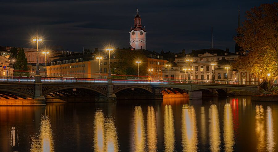 Riddarholmen Church and bridge lights reflecting on water at night in Stockholm