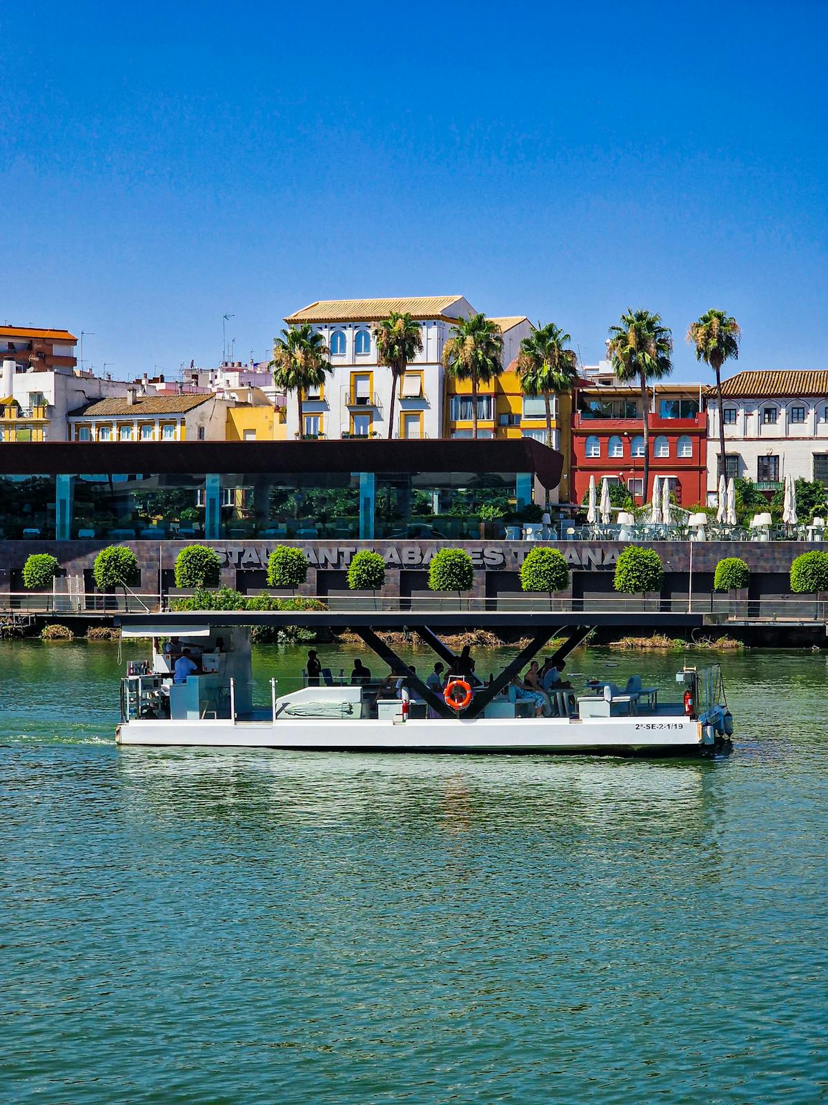A boat on the Guadalquivir River passing colorful buildings along the Seville waterfront