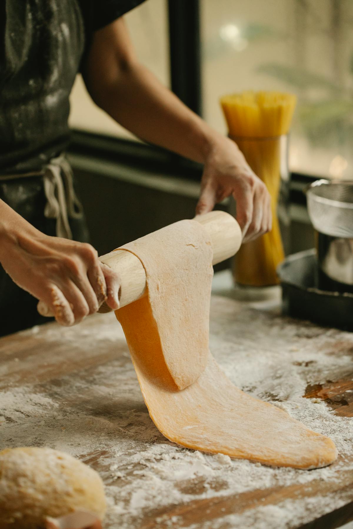 Woman rolling fresh egg pasta dough on a flour-covered wooden table with a rolling pin