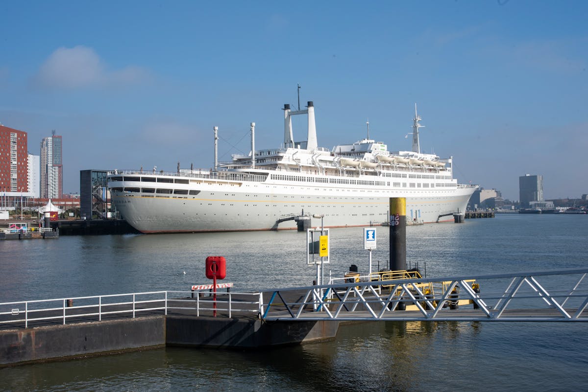 Large cruise ship docked at a port in Rotterdam under a clear blue sky