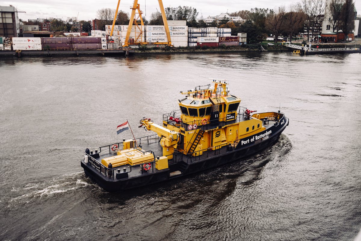 A tugboat on the river at the Port of Rotterdam with containers and cranes in the background
