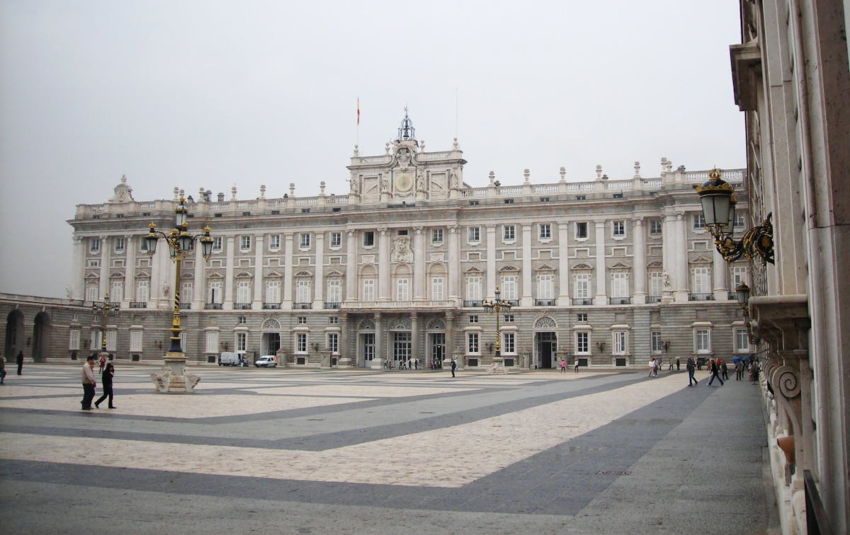 The Royal Palace of Madrid seen from the historical plaza with visitors walking below
