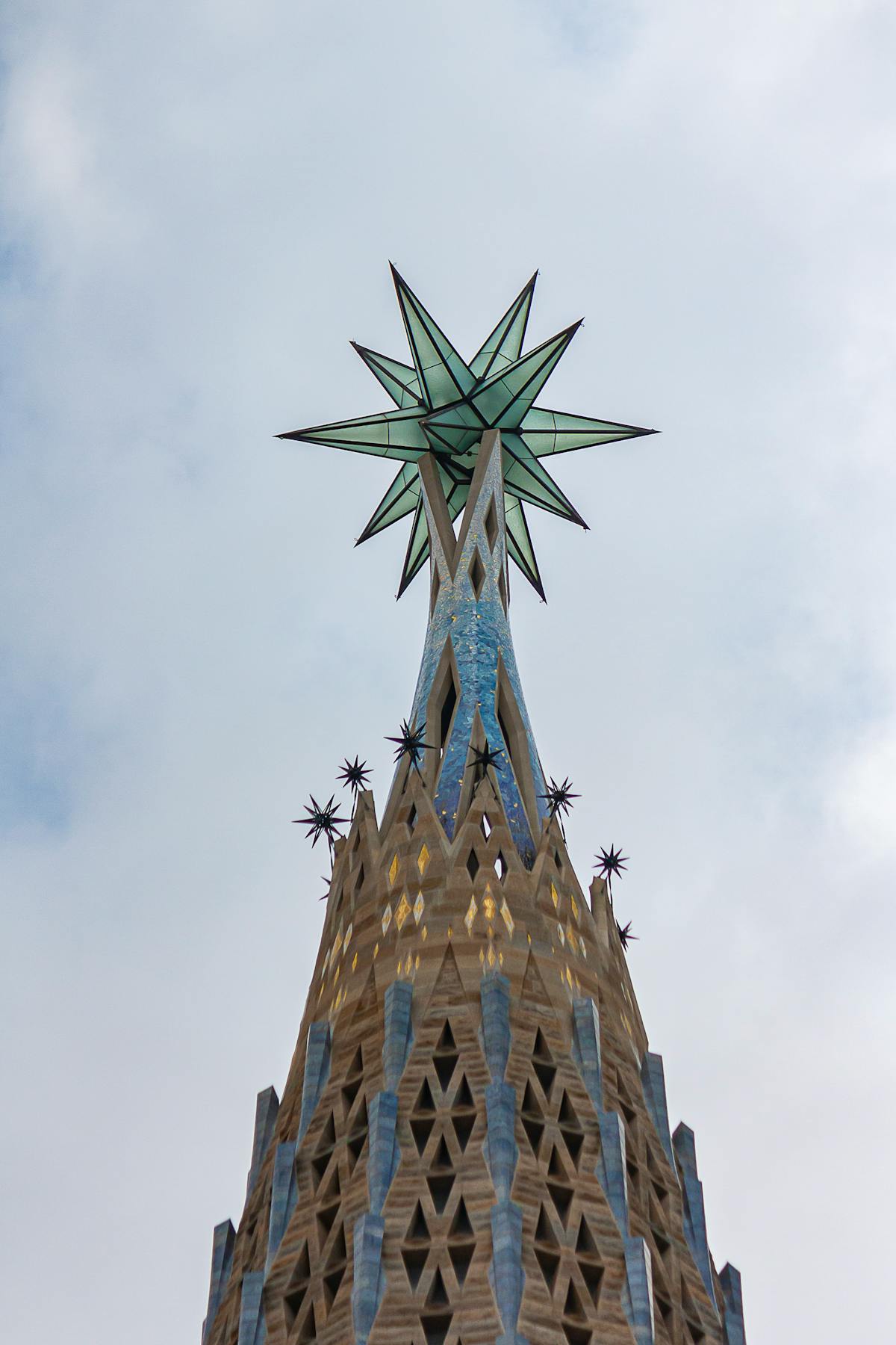 Close-up of the iconic Sagrada Familia spire topped with an illuminated star against cloudy sky