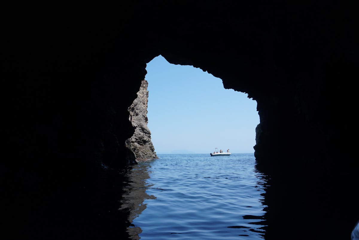 A small motorboat navigating into the entrance of a sea cave with light reflecting off the water
