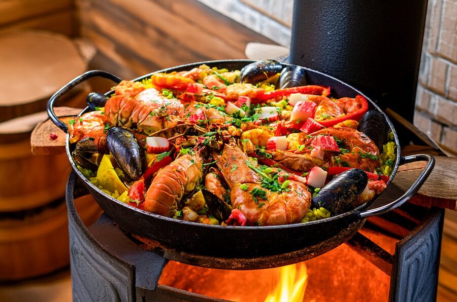Seafood paella sizzling over an open flame with colorful ingredients