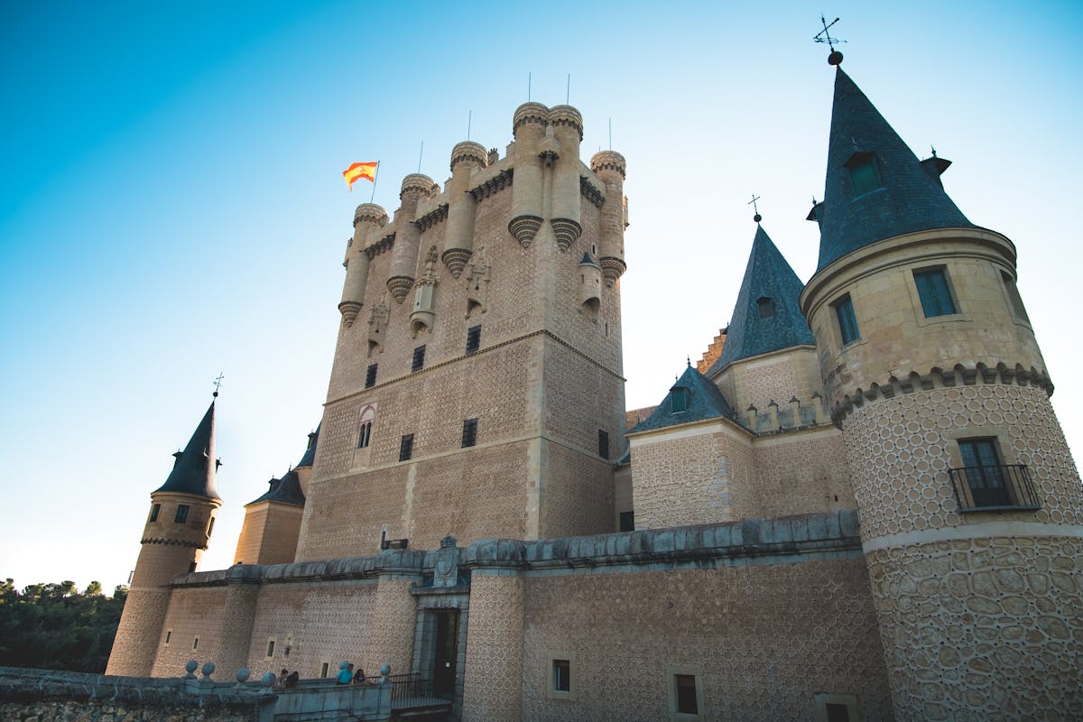 The Alcazar of Segovia castle perched on a rocky cliff with its distinctive turrets against a blue sky
