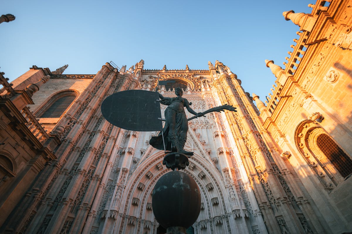 The grand stone facade of the Seville Cathedral with carved archways and Gothic detailing