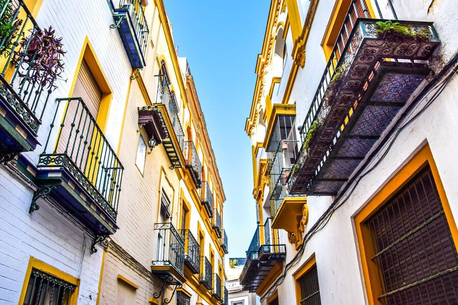 Narrow street with colourful buildings and flower-covered balconies in Seville Spain