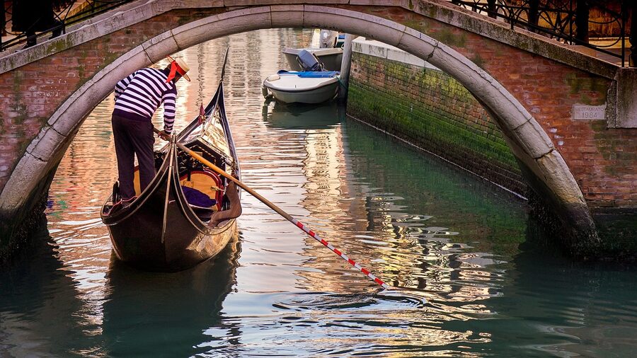 Gondolier steering gondola under a bridge in Venice canal