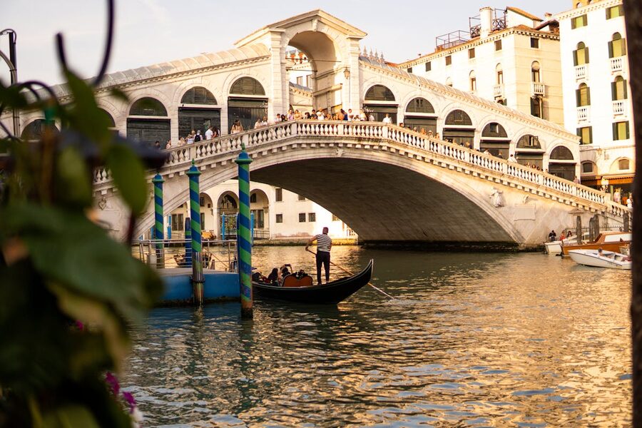 Gondola navigating Grand Canal near Rialto Bridge at sunset in Venice