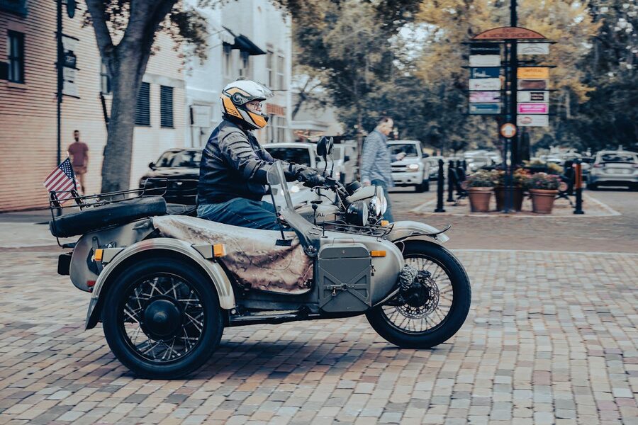 Man riding vintage motorcycle with sidecar on cobblestone city street