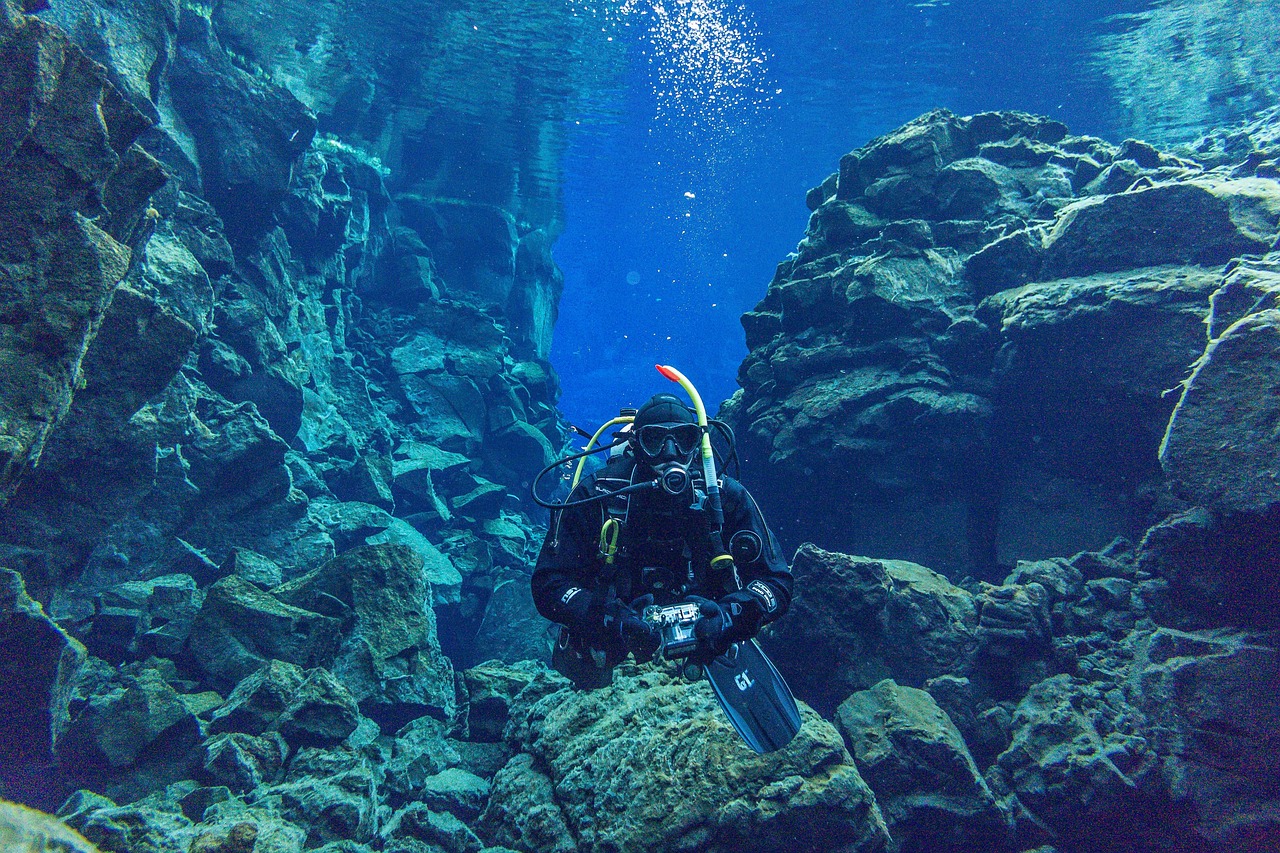 Scuba diver in drysuit swimming through Silfra fissure between tectonic plates with crystal clear blue water