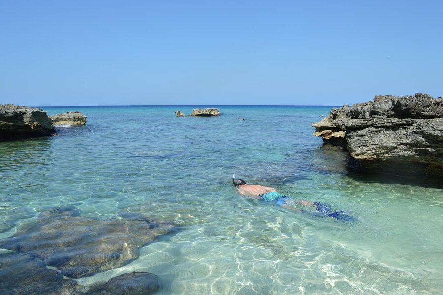 Person snorkeling in crystal clear waters near rocky formations