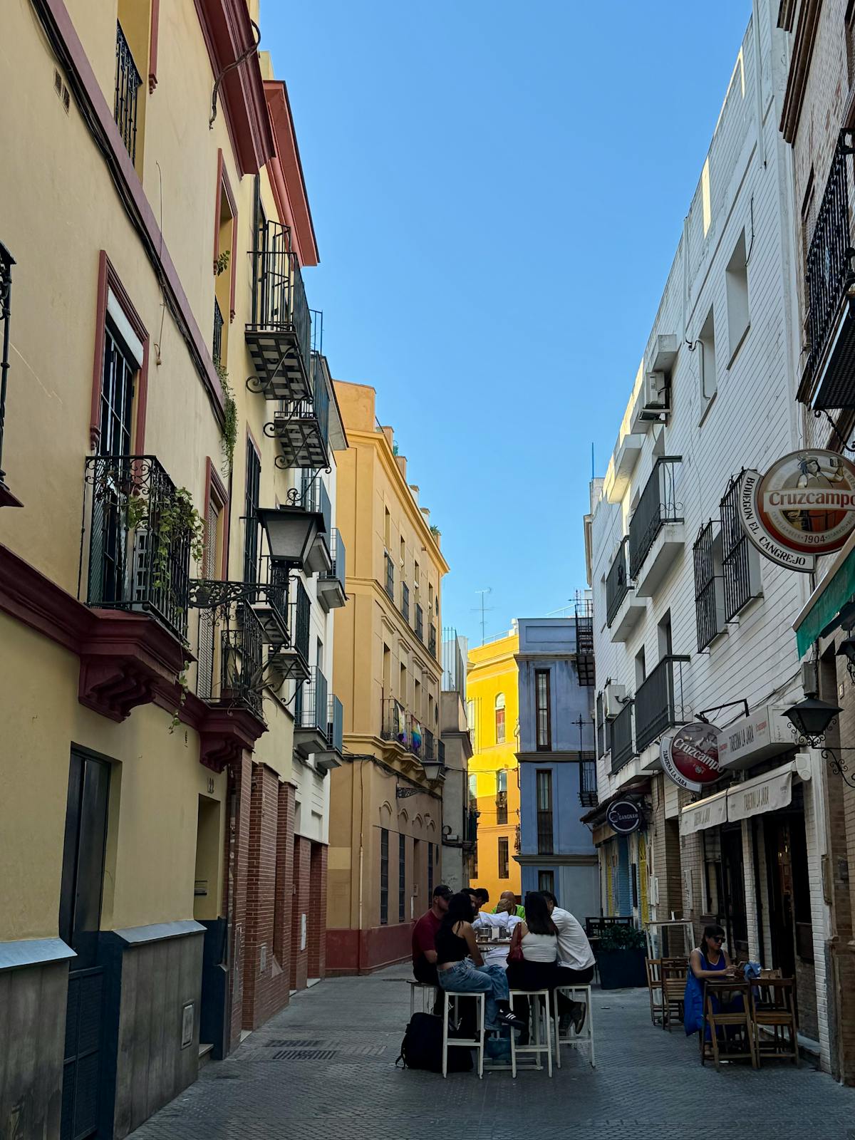 People dining outdoors on a colorful street in Spain surrounded by historic buildings