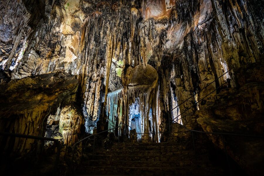Wide view of illuminated cave interior showing towering stalactite and stalagmite formations