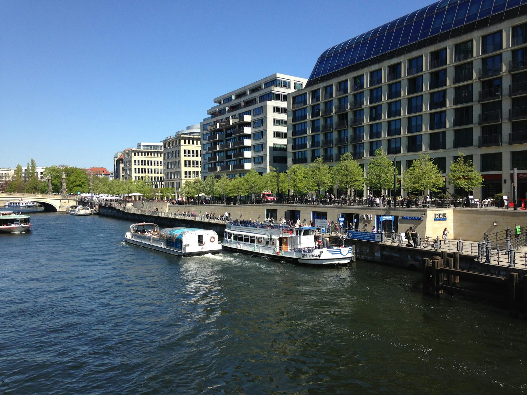 Tour boats lined up along the Spree River with modern Berlin architecture behind them