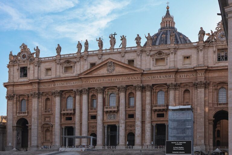 The grand facade of St. Peters Basilica with its towering columns and statues against a clear sky