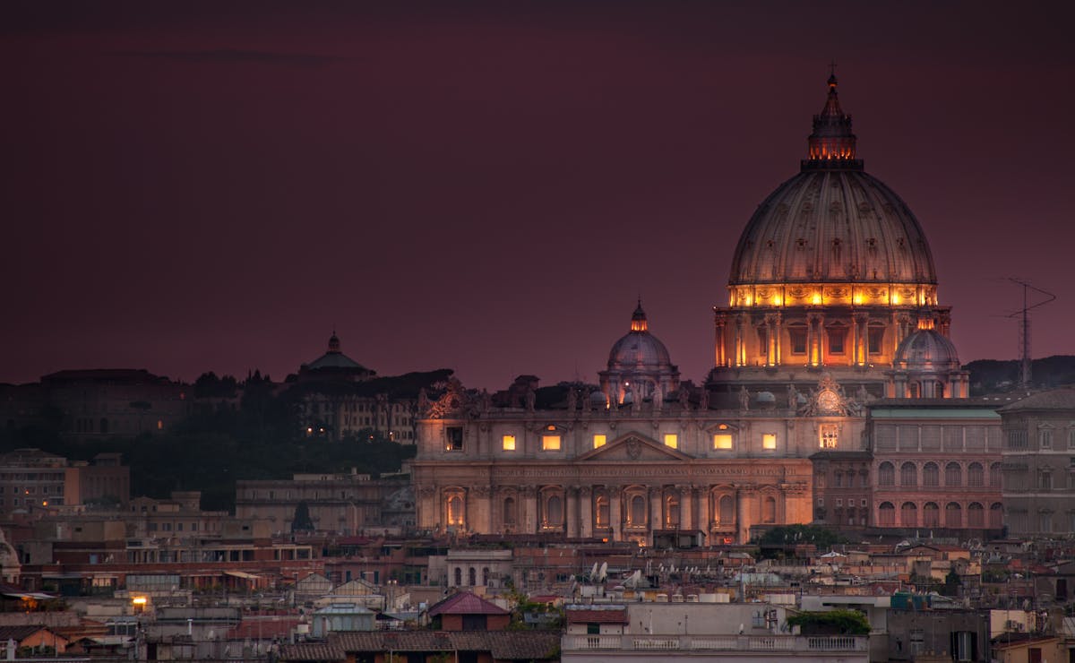 St. Peters Basilica dome and facade lit up at night against a dark blue sky