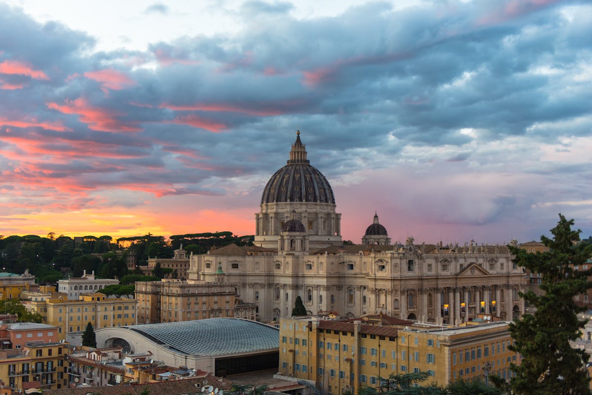 St. Peters Basilica dome silhouetted against an orange and pink sunset sky