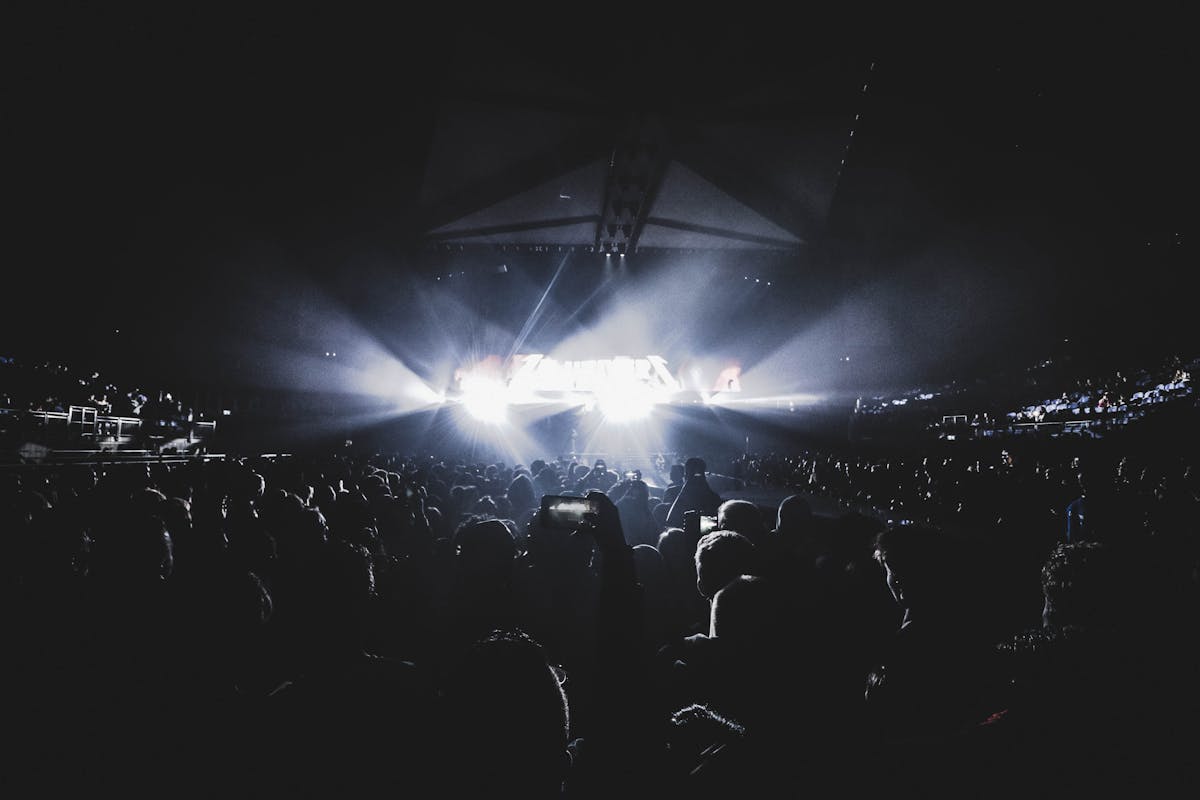 Concert crowd in dark stadium with stage lights illuminating the arena