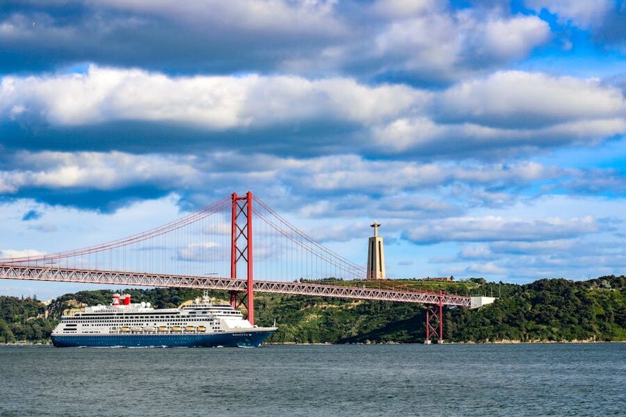Cruise ship sailing under 25 de Abril Bridge with Cristo Rei in background