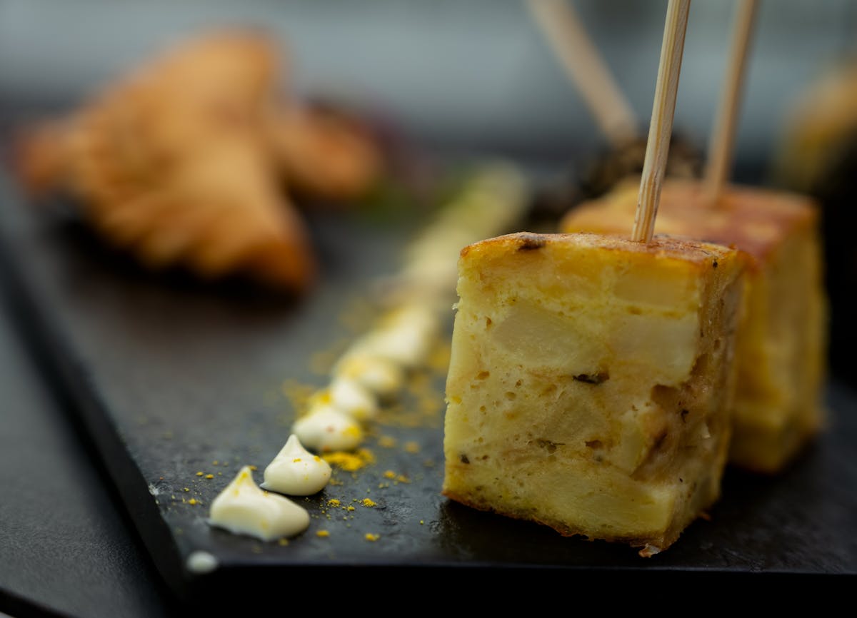 A wedge of Spanish tortilla served with aioli on a dark slate plate