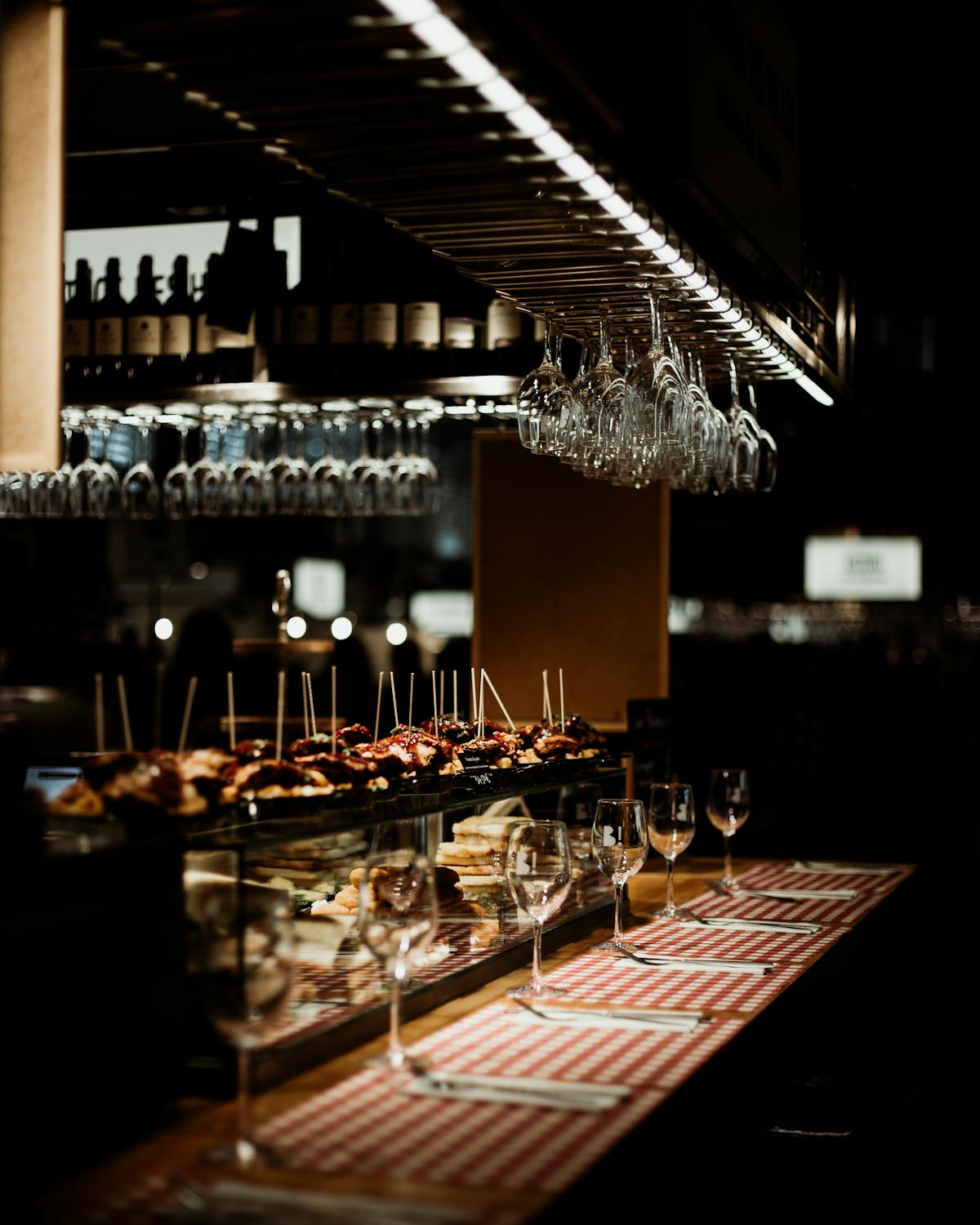 Tapas plates and wine glasses on a wooden bar counter in a dimly lit restaurant