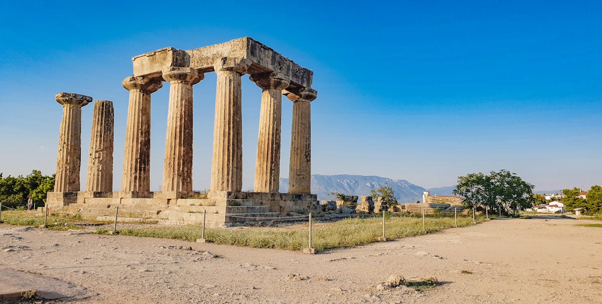Ancient Corinth Temple of Apollo columns bathed in sunlight with mountains behind